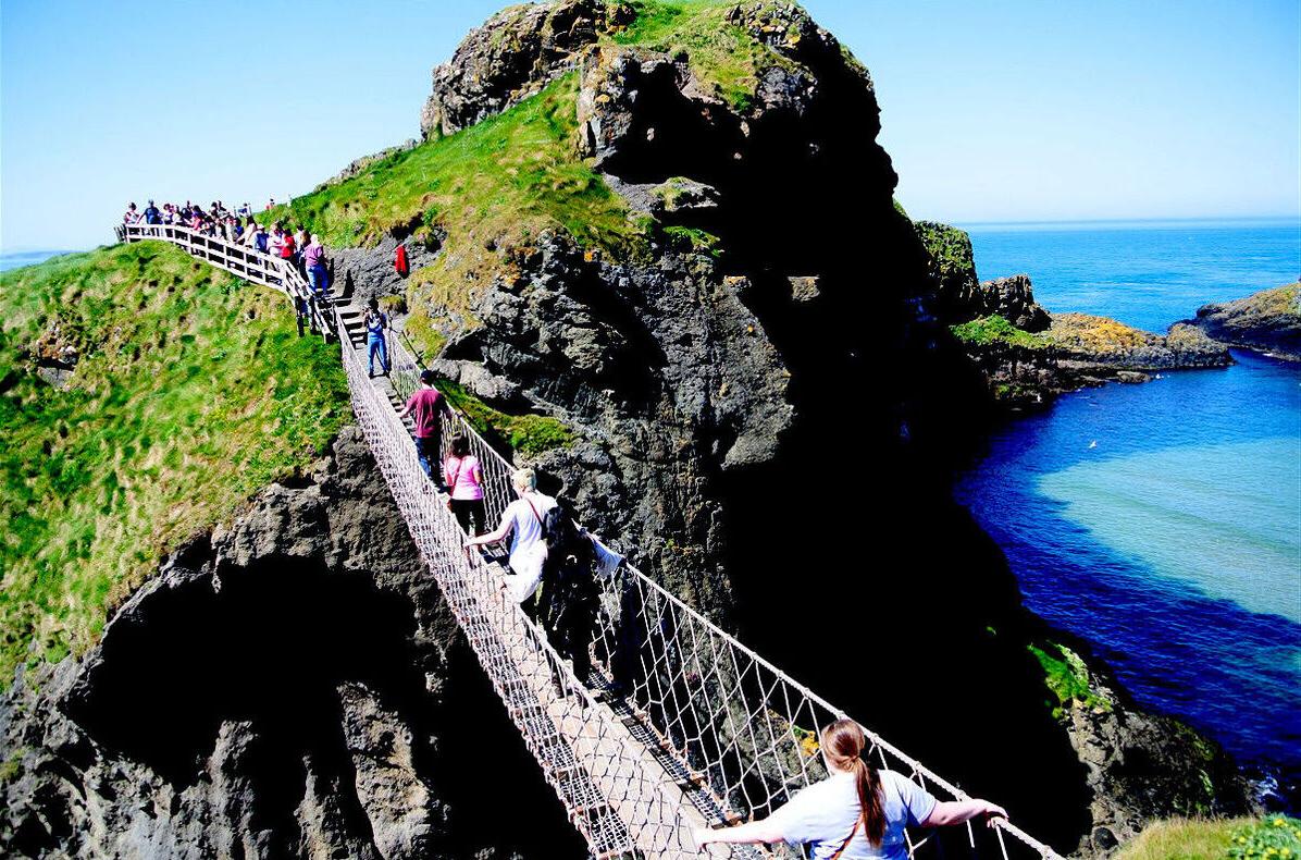 在爱尔兰的一个岩石海岸地区，游客们正穿过一座跨越鸿沟的绳桥